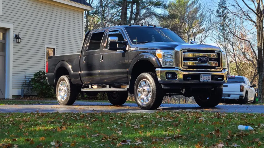 Black Ford Super Duty pickup truck parked in driveway next to house and white sedan.