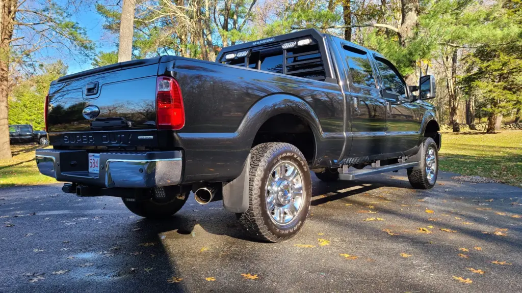 Black Ford Super Duty pickup truck parked in driveway, rear three-quarter view showing bed and chrome wheels.