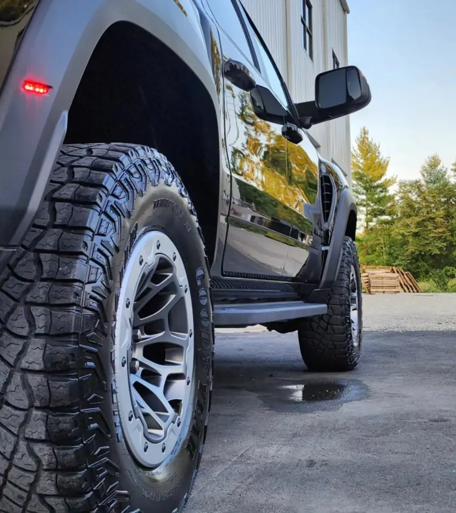 Close-up of a black pickup truck's front wheel with custom silver alloy rim and all-terrain tire.
