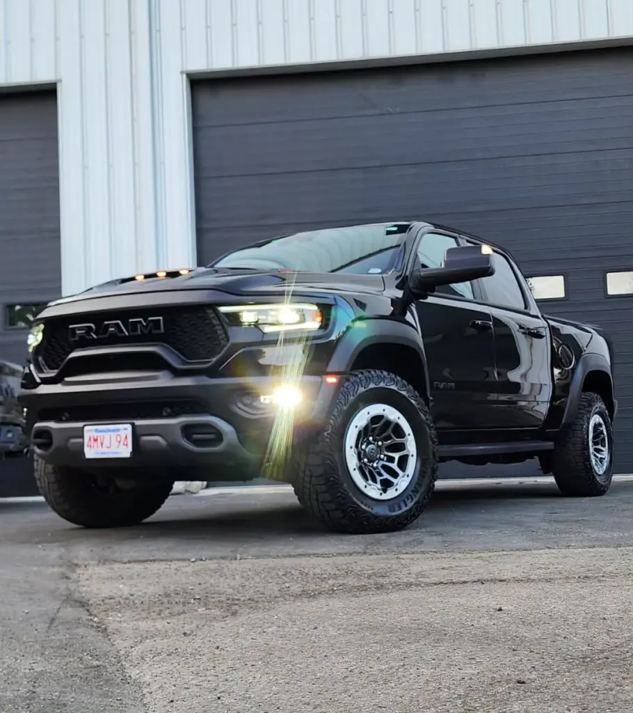 Black RAM pickup truck with illuminated headlights parked in front of a detailing facility garage.