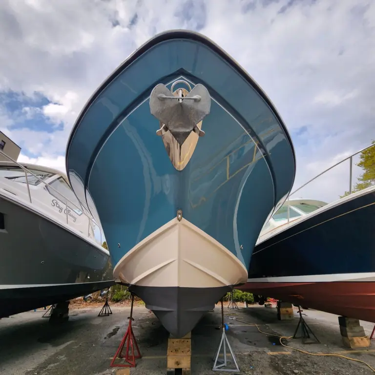 Front view of a blue boat with polished anchor and hardware mounted on the bow, in dry dock.