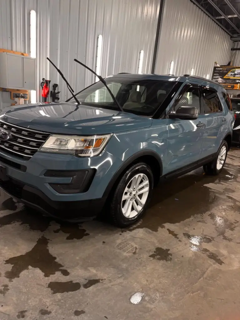 Blue Ford Explorer SUV with both front doors open in an industrial garage with corrugated metal walls.