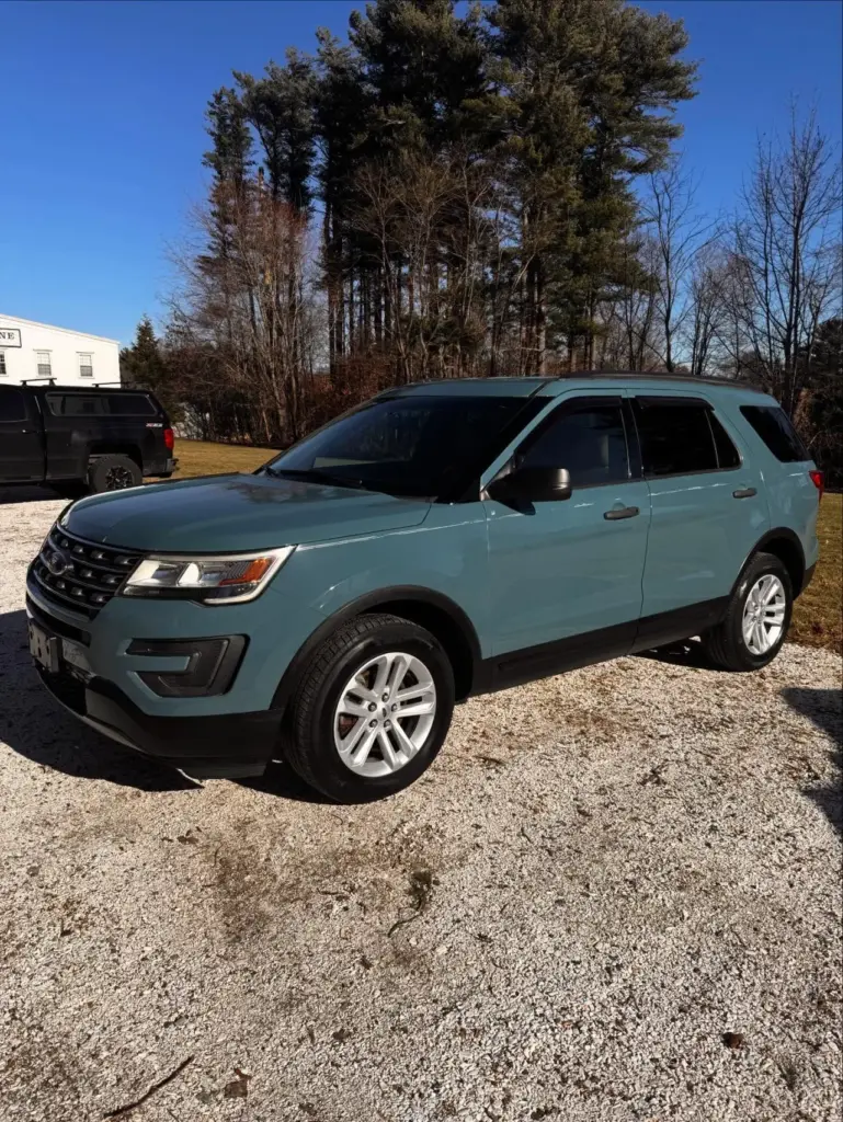 Blue Ford Explorer SUV parked on gravel lot with trees and white building in background.