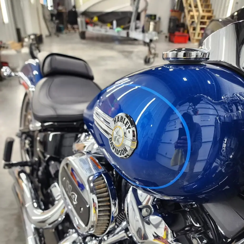 Close-up of a blue Harley-Davidson motorcycle fuel tank with chrome badge and emblem in a garage.