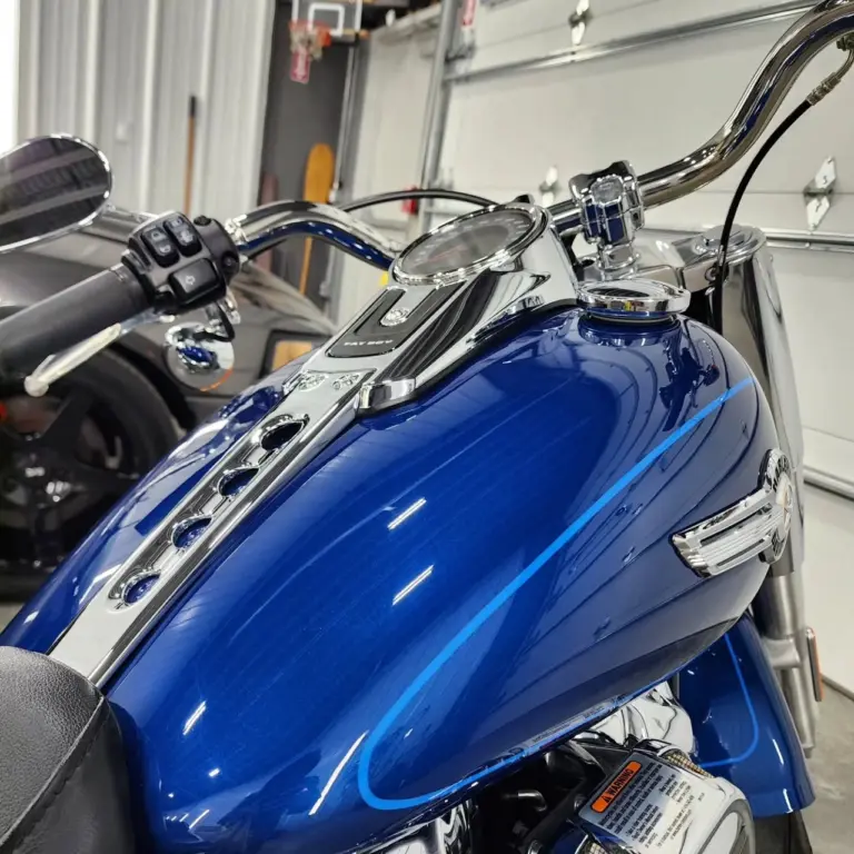 Close-up of a blue Harley-Davidson motorcycle fuel tank and chrome handlebars in a garage.