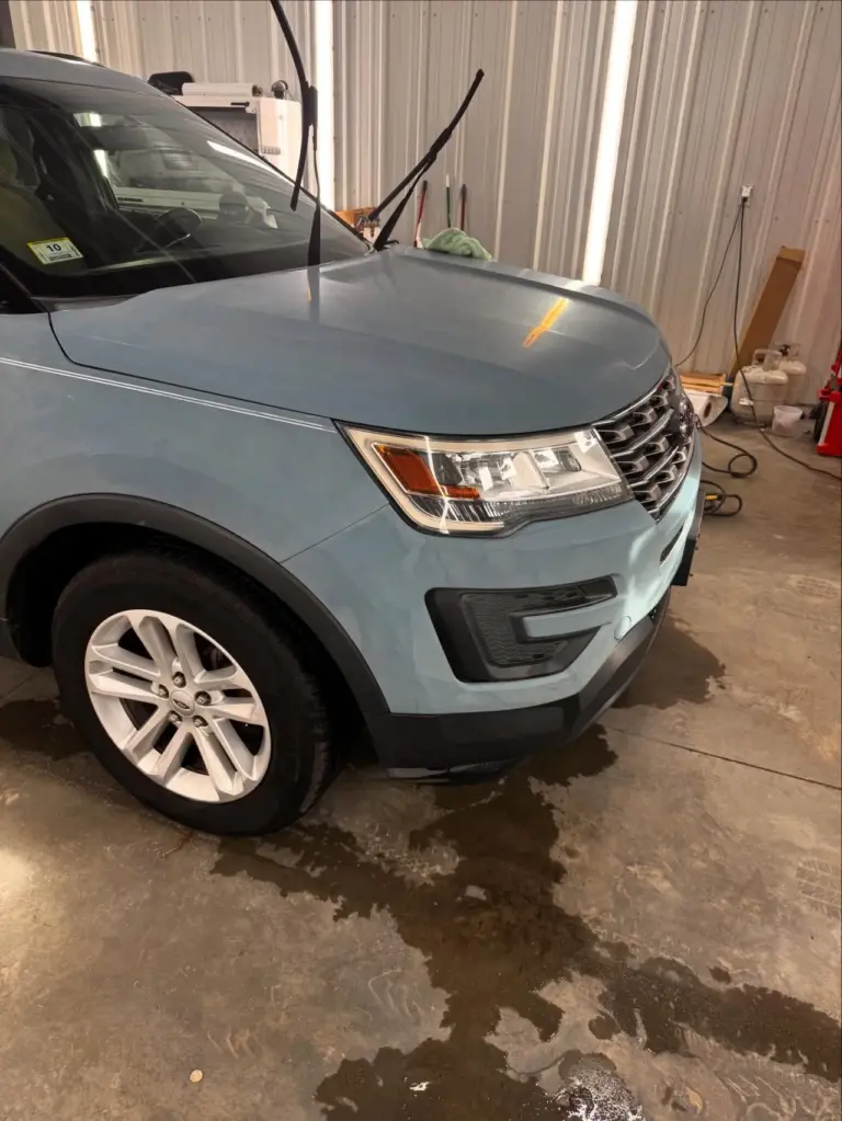 Blue SUV with hood and headlight visible in an indoor garage with corrugated metal walls.