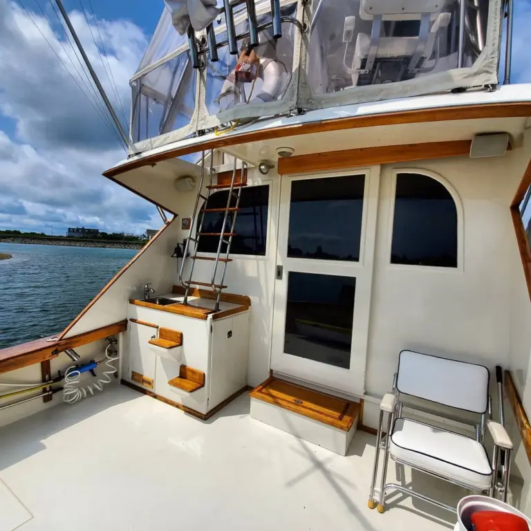 Aft deck of a cabin cruiser with wooden stairs leading to upper helm, cabin door, and stacked chairs moored in Pembroke waters.