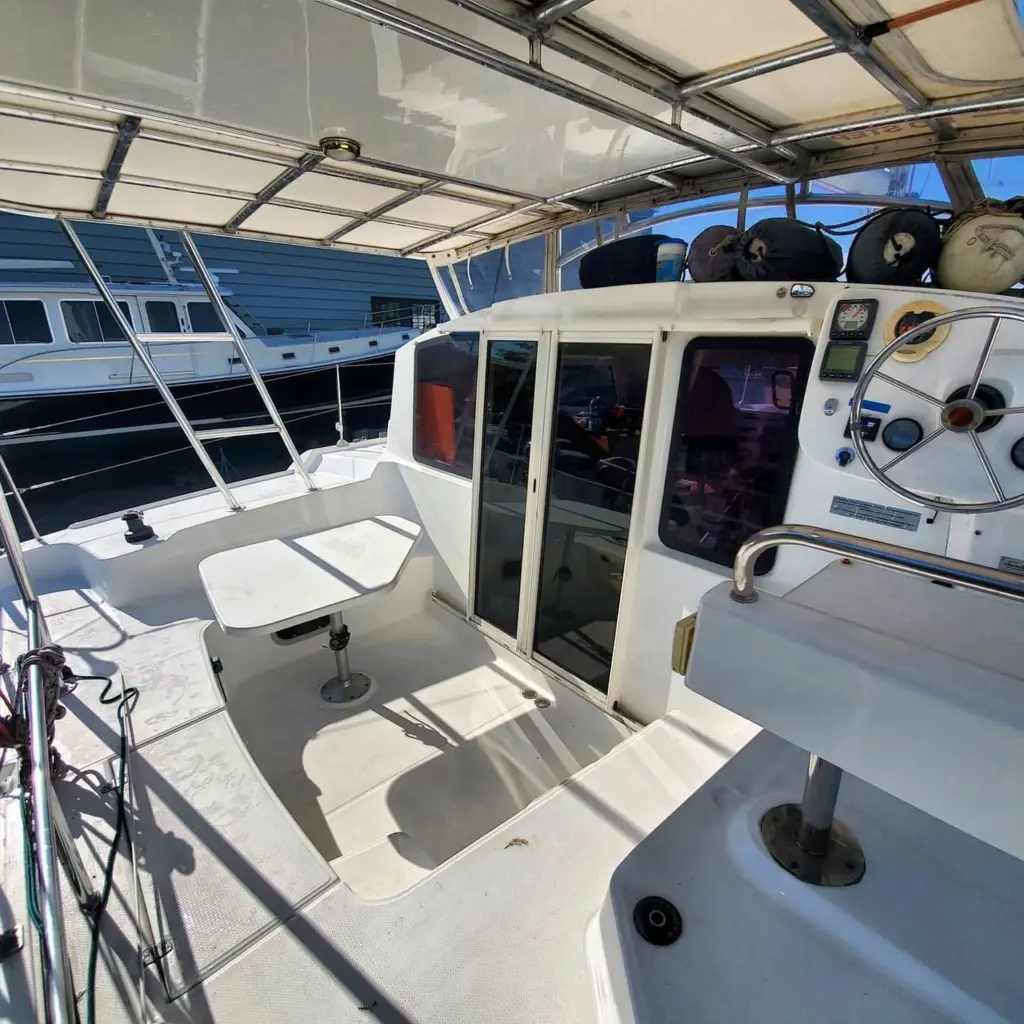 Aft deck of a white cabin cruiser with helm station, bimini top, and moored boats visible in background.