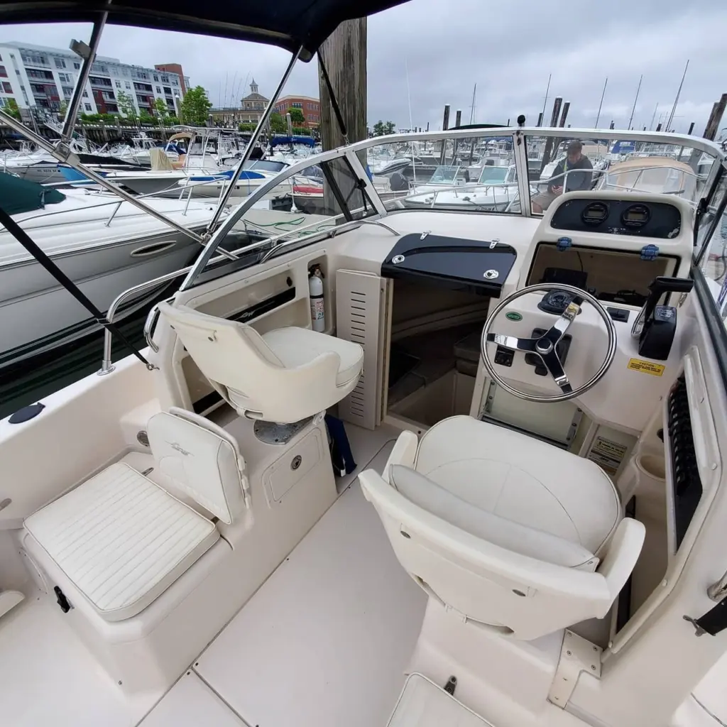 Interior view of boat cabin with cream-colored seating, steering wheel, and navigation console overlooking marina.