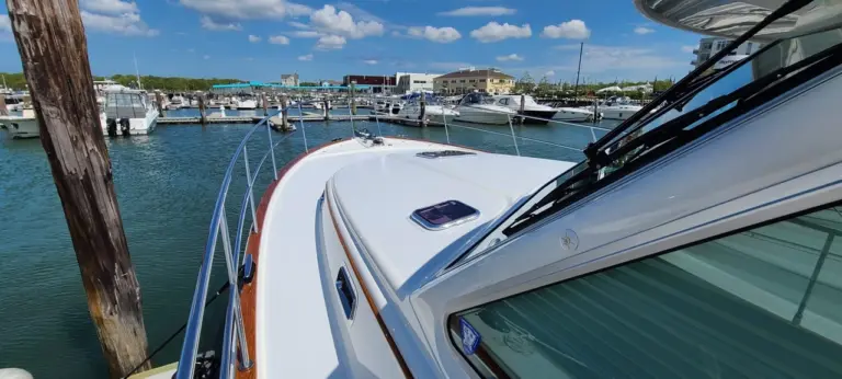 Polished white cabin roof of a boat docked at a marina with other vessels and waterfront buildings visible.