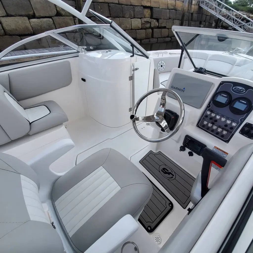 Boat cockpit interior showing helm wheel, Garmin navigation display, control panel, and gray upholstered seating.