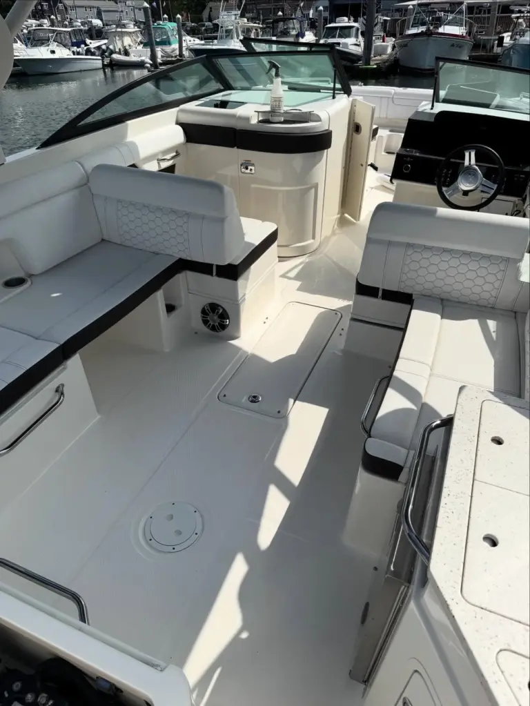 Open cockpit of white boat with white upholstered seating, helm controls, and raised windshield at marina.