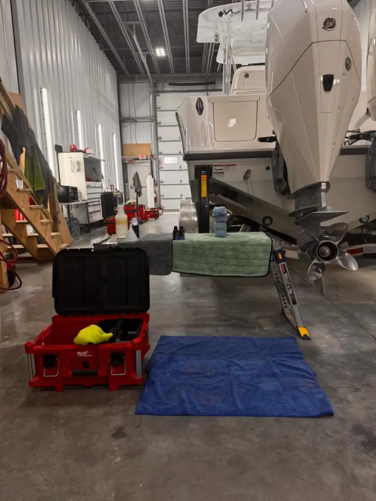 Interior view of a detailing garage with protective floor mats, tool storage, and white cabin cruisers on trailers.