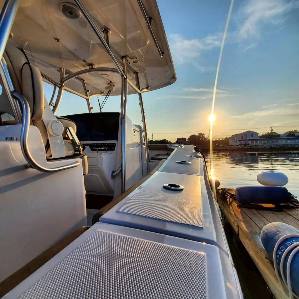 Boat gunwale and side deck at sunset with mooring lines and waterfront buildings in background.