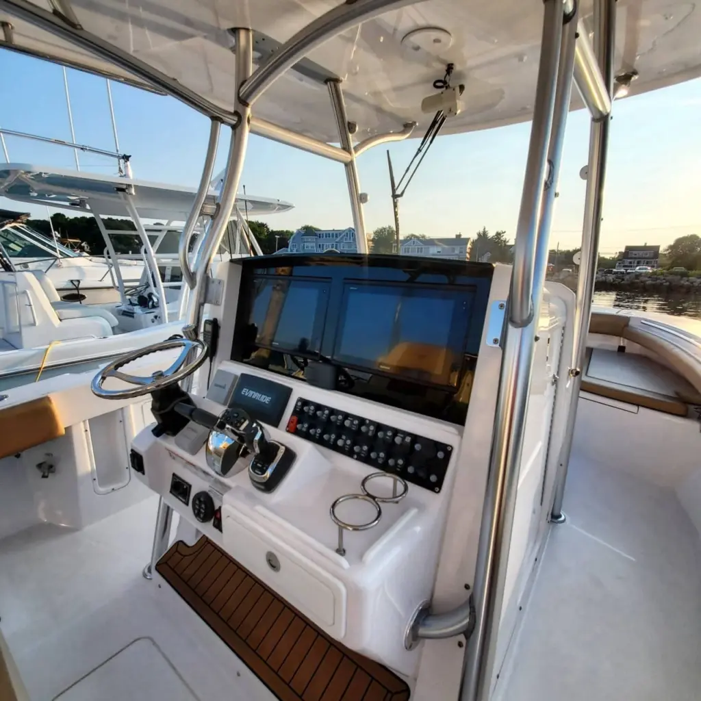 Boat helm station with Evinrude display screen, control panel, and steering wheel inside cabin with waterfront view.