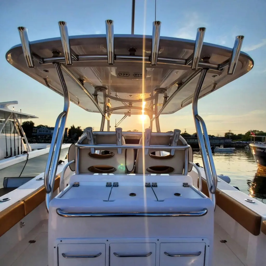 Under-view of a boat's T-top canopy with chrome support poles, passenger seating, and storage compartments at sunset on Pembroke waterfront.