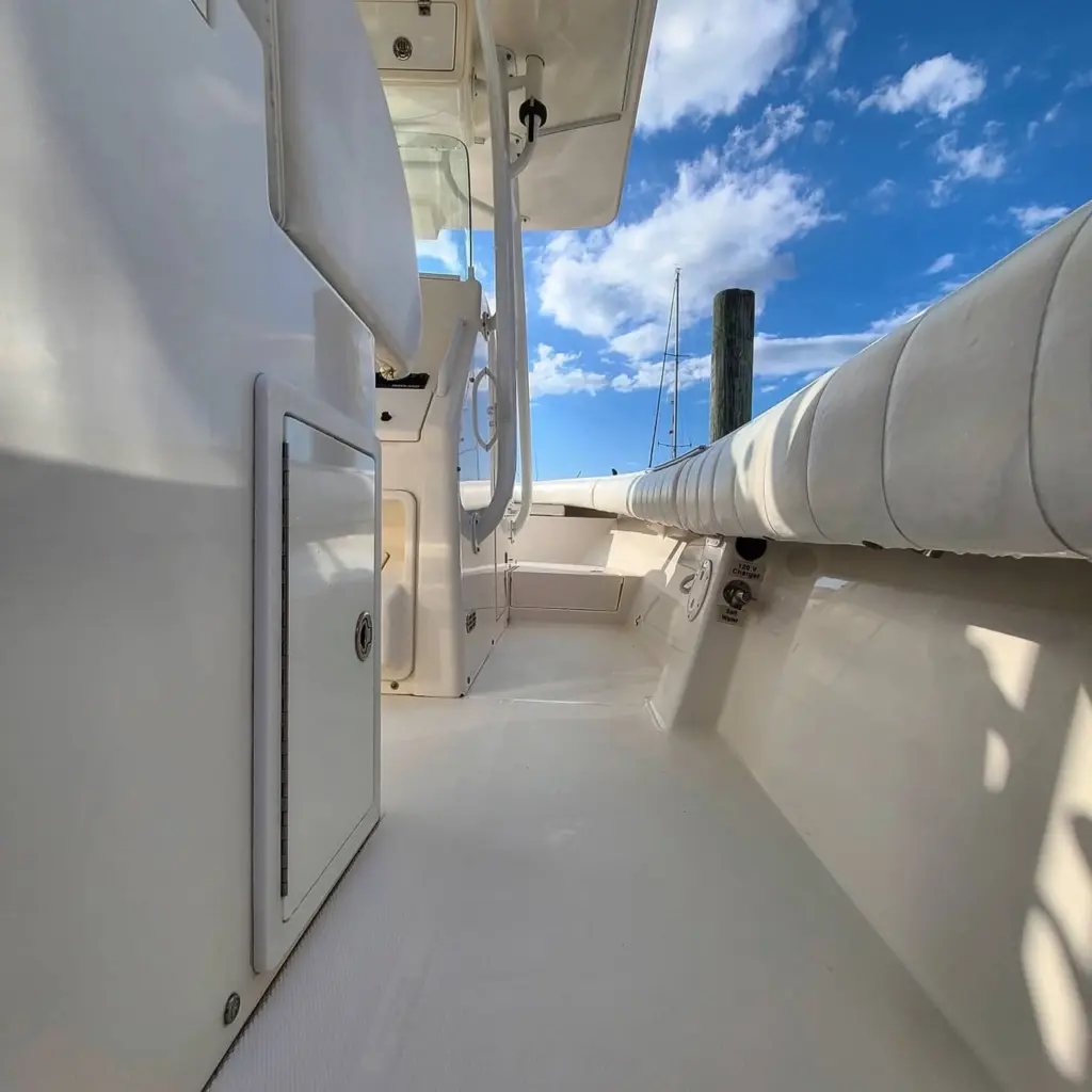 Interior side walkway of a white cabin cruiser docked at a marina, showing cabin door and mooring pole.