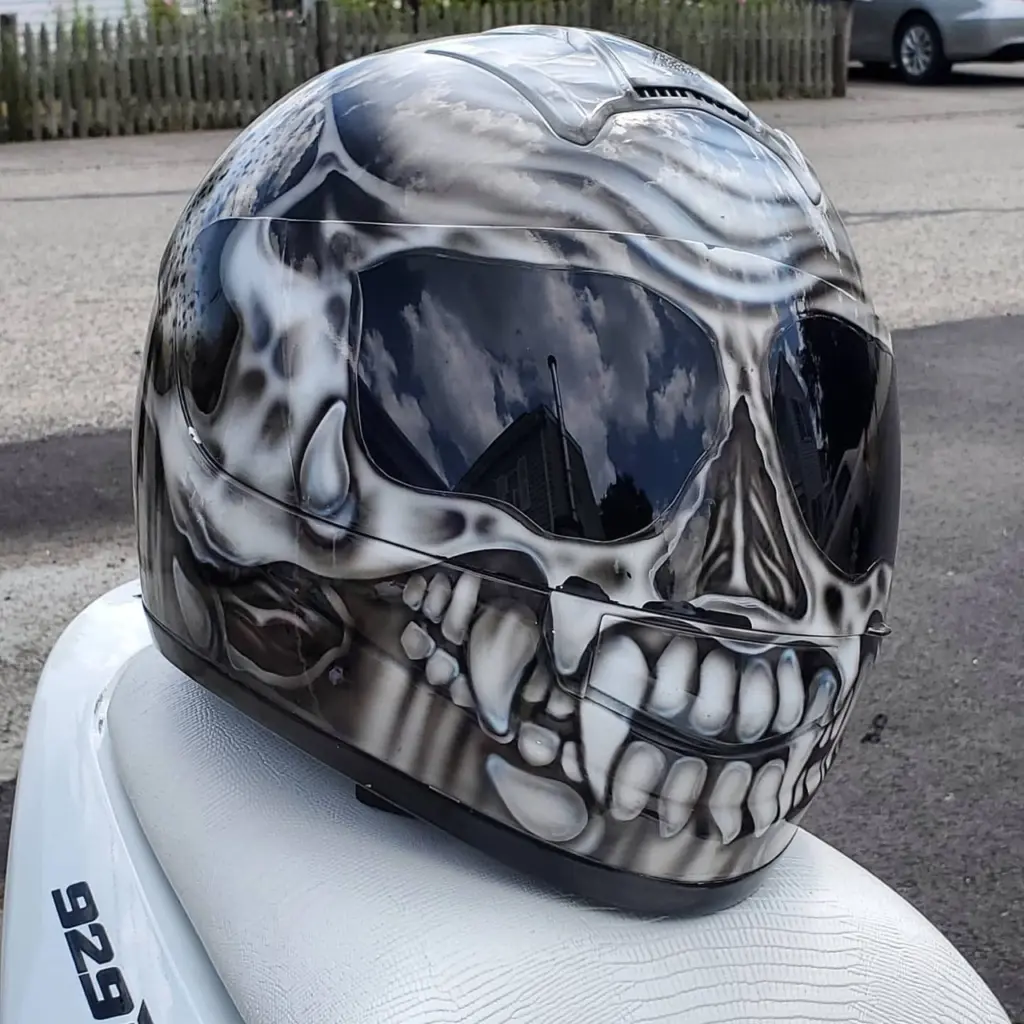 Close-up of a black and white airbrushed skull design motorcycle helmet on a white seat.