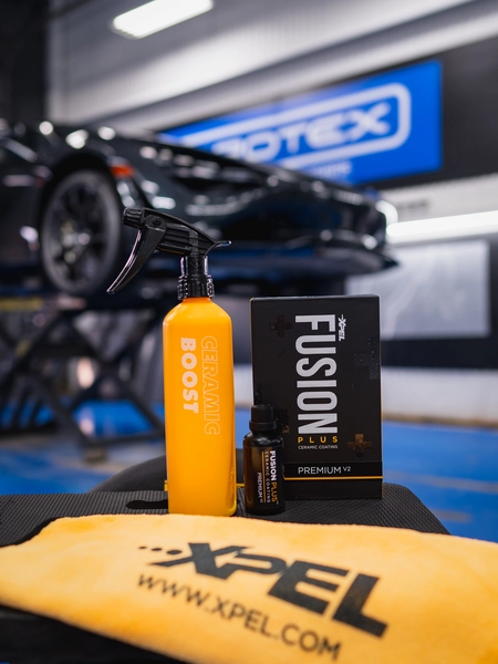Detailing products including Boost spray bottle and Fusion Plus box displayed in front of a vehicle in a detail shop.