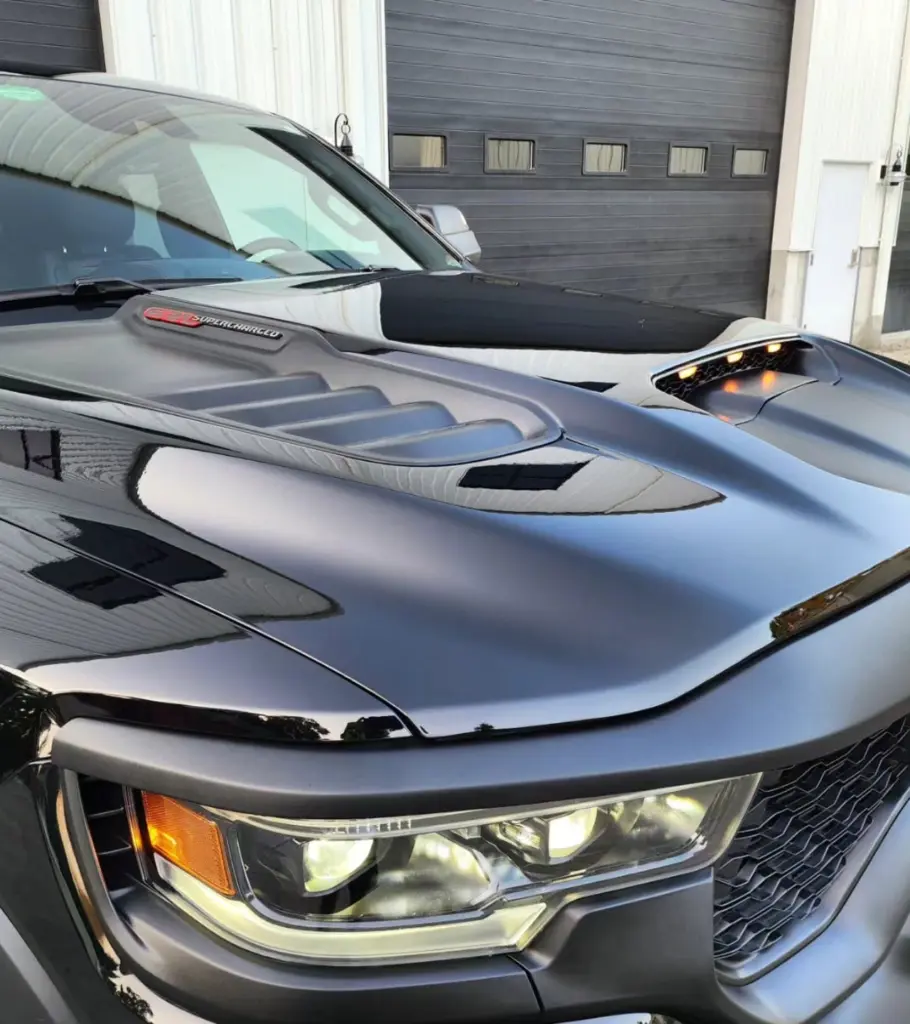 Close-up of a Dodge Charger hood and headlight assembly in a garage with other vehicles visible.