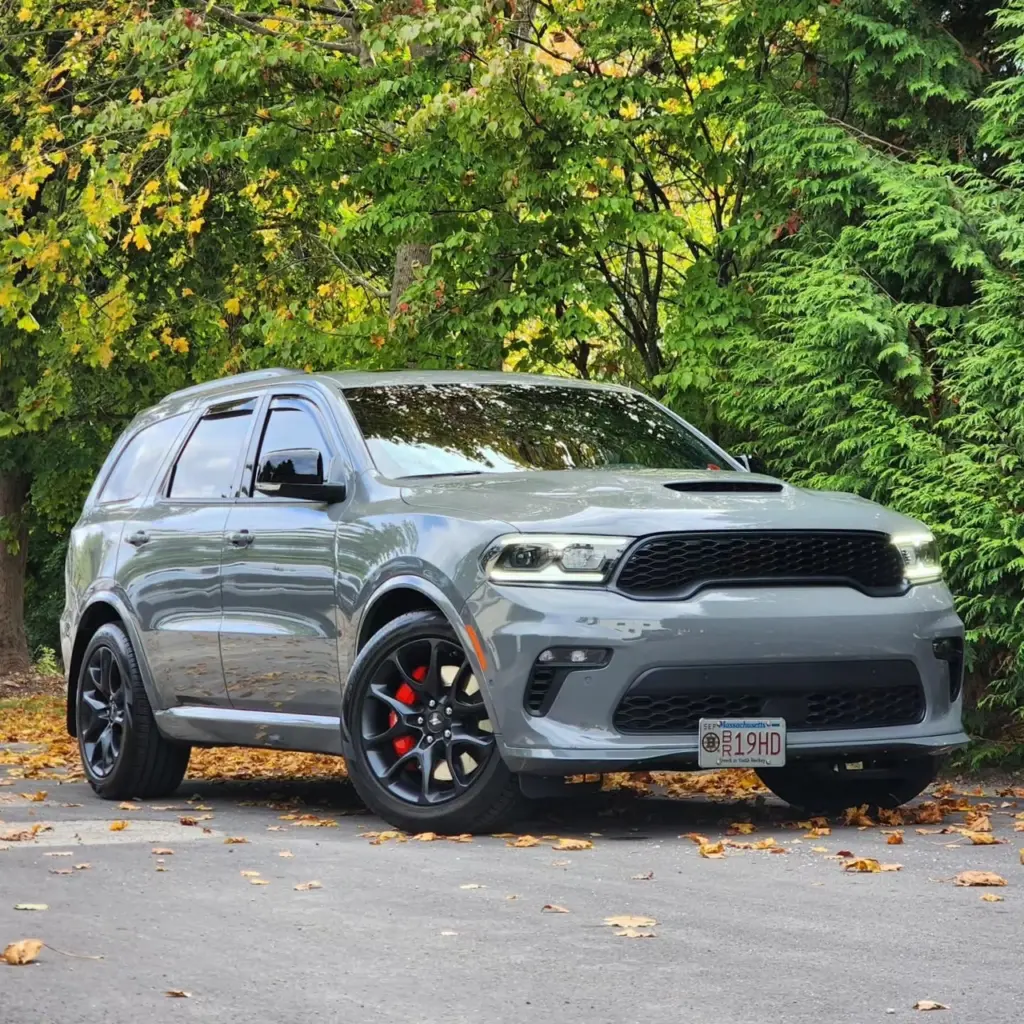 Silver Dodge Durango SRT SUV parked on driveway with fall foliage in background.
