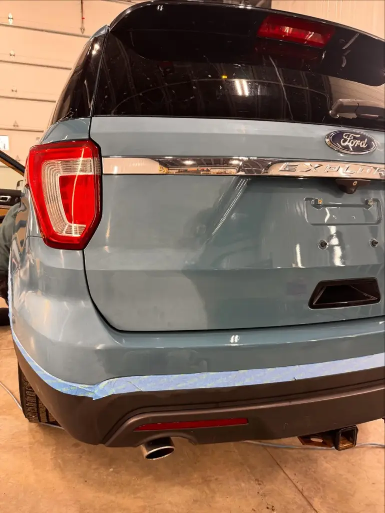 Rear quarter view of a gray Ford Explorer SUV showing taillight and rear bumper in a garage.