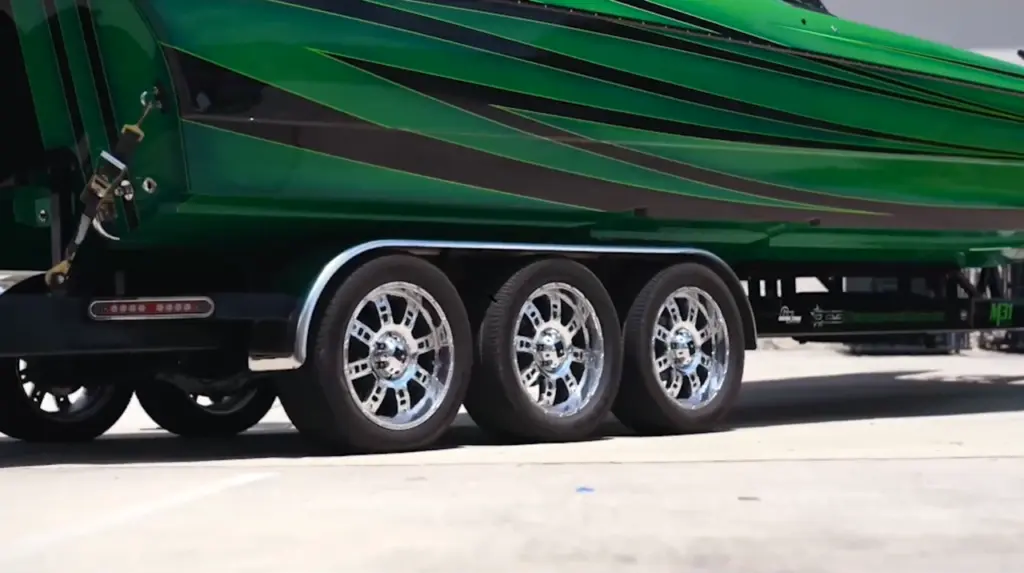 Close-up of three polished chrome wheels on the side of a green semi-truck trailer.