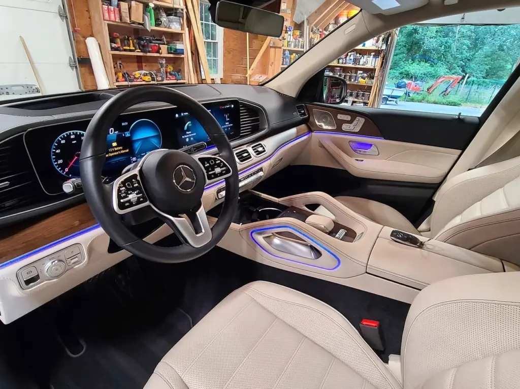Mercedes-AMG interior with black steering wheel, tan leather seats, blue ambient lighting, and digital dashboard.