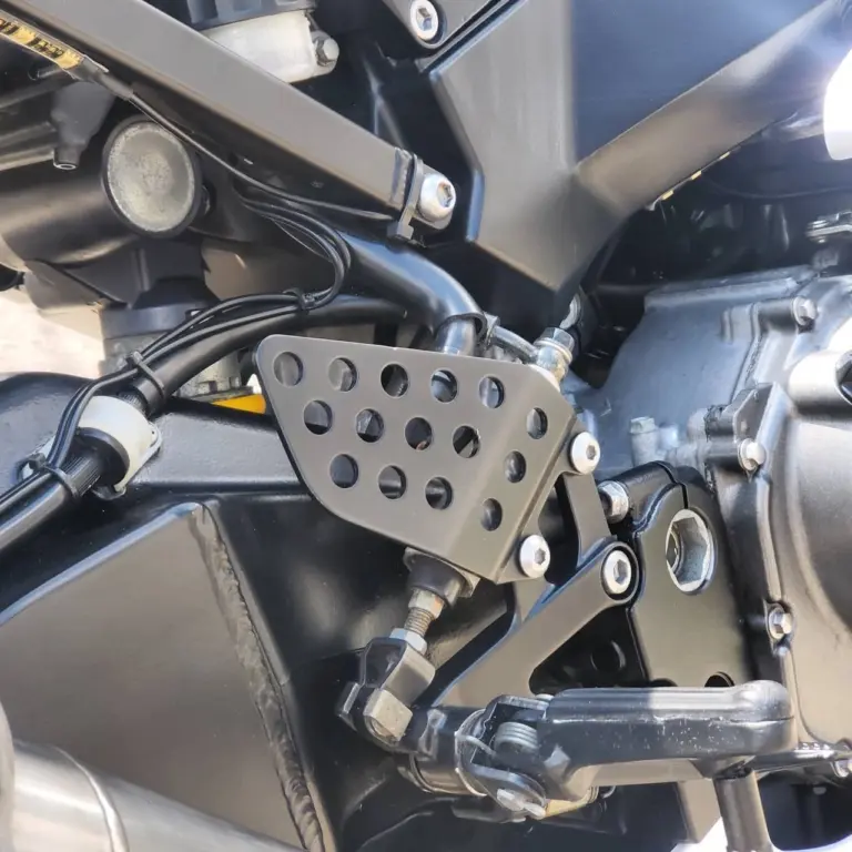 Close-up of custom motorcycle foot pegs and brake lever assembly with stainless steel perforated platform.