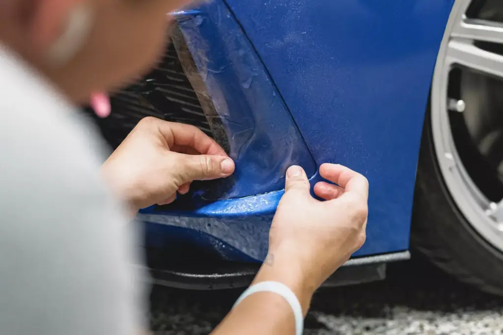Technician applying protective film to the side of a blue vehicle.