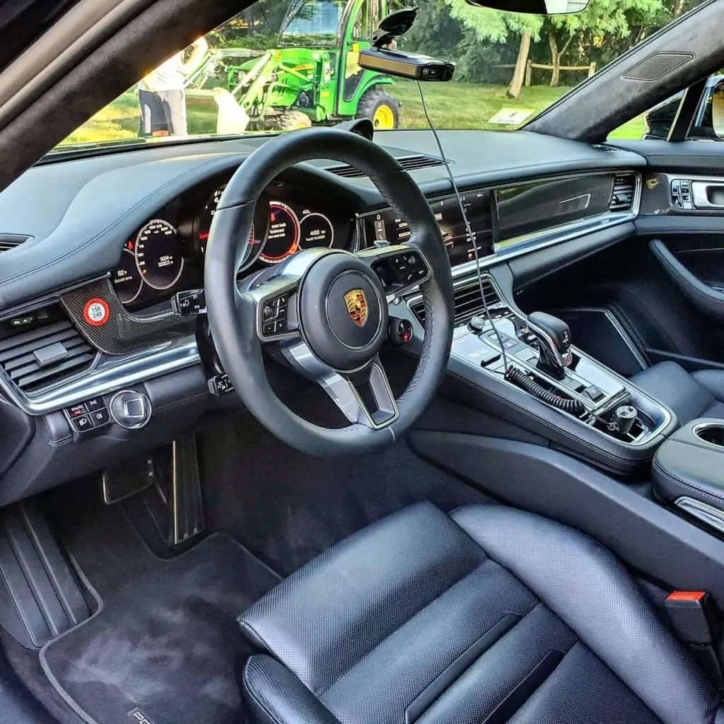 Interior view of a Porsche showing black leather steering wheel, dashboard gauges, and center console.