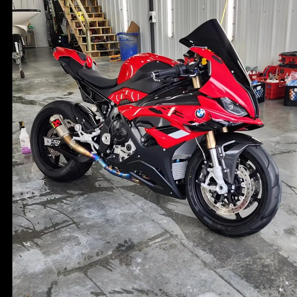 Red and black BMW sportbike with custom exhaust system in detailing garage.