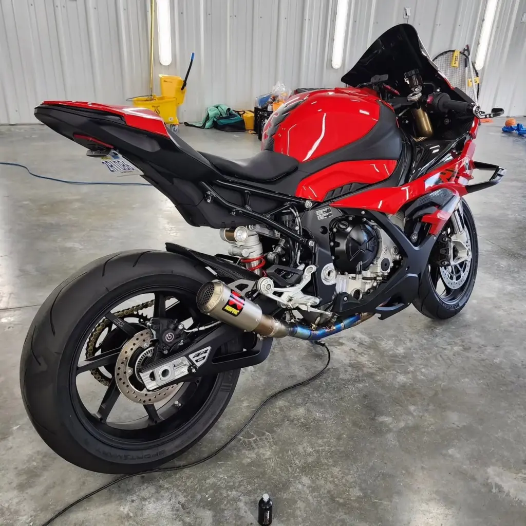 Red and black sportbike with custom exhaust system in garage workshop.