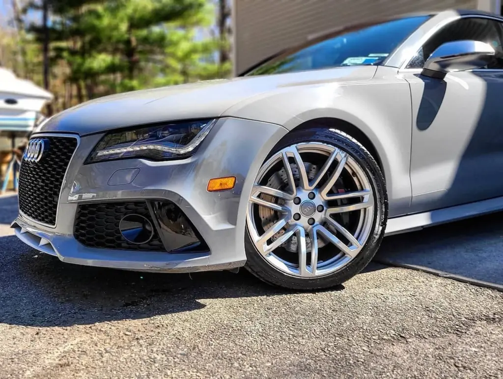 Silver Audi RS7 sports car with polished alloy wheels and open door, parked in driveway.