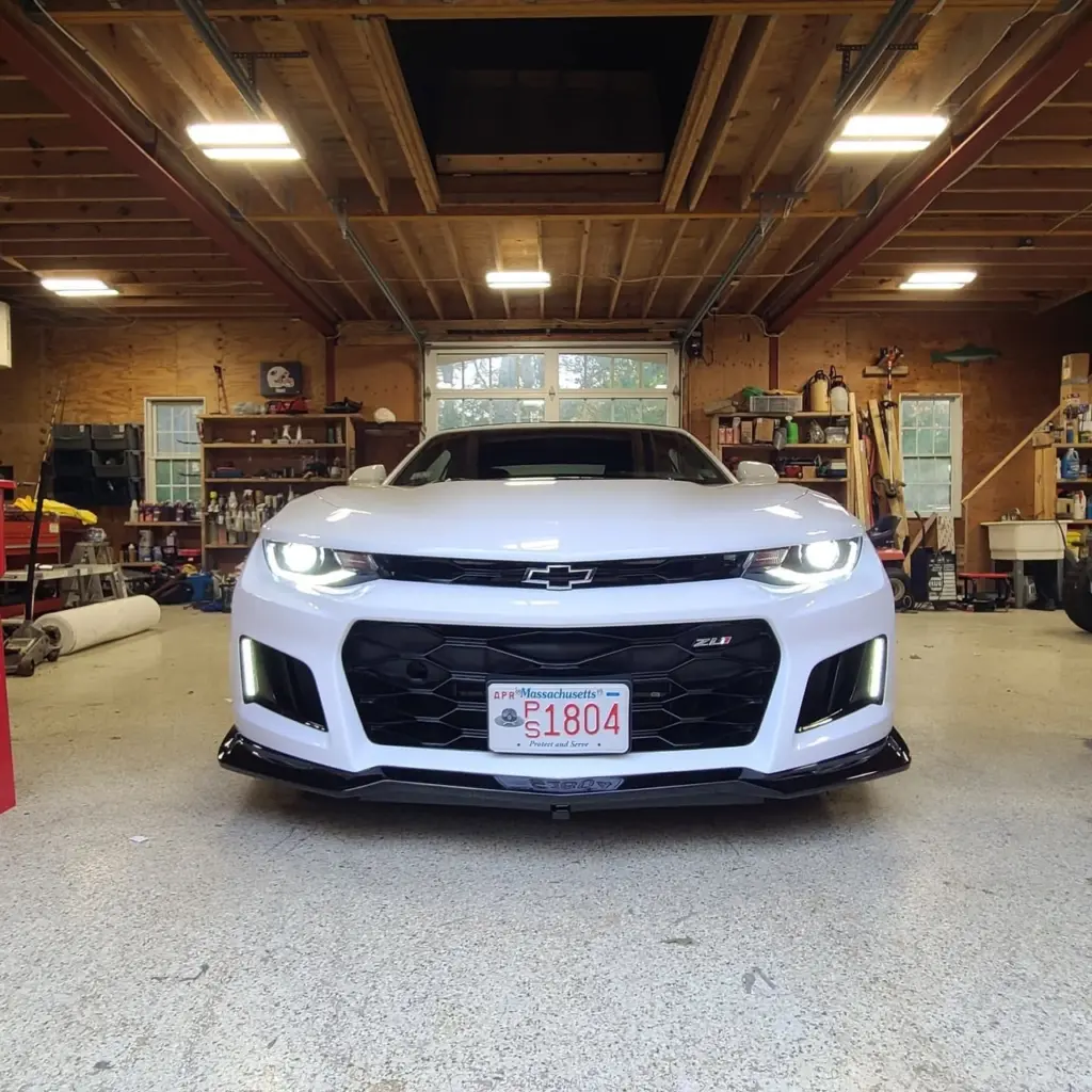 White Chevrolet Camaro ZL1 parked front-facing in a wooden garage workshop.