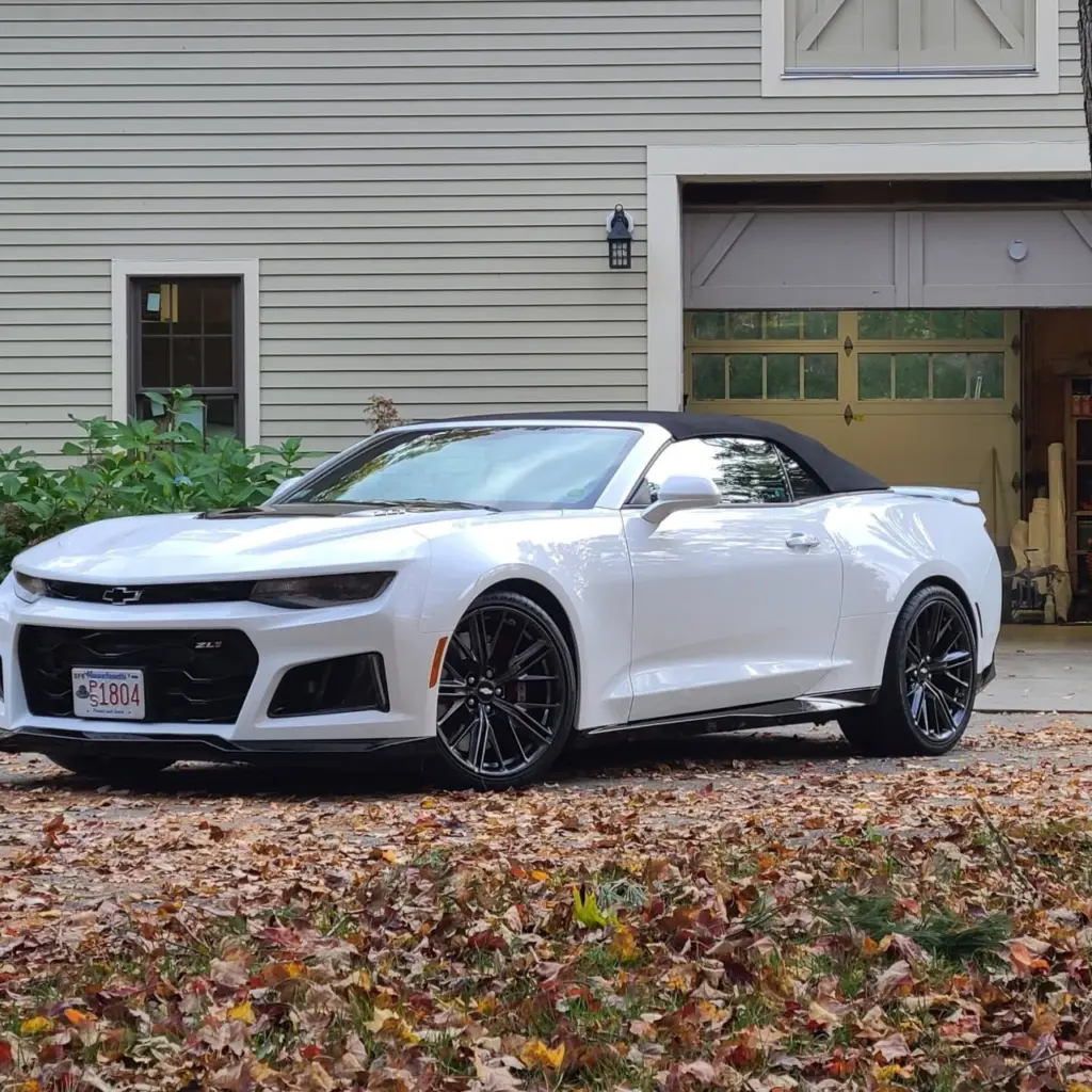 White Chevrolet Camaro ZL2 convertible with black top parked in driveway with garage and house in background.