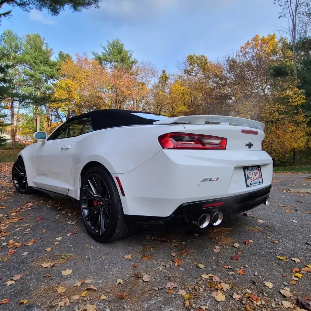 White Chevrolet Camaro ZL1 convertible with black top, dual exhaust, and black wheels parked on driveway.