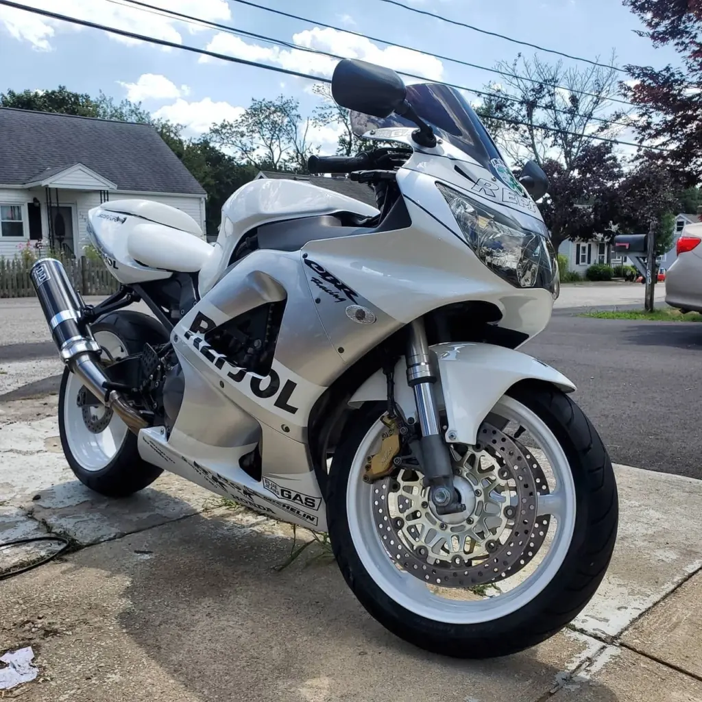 White sport motorcycle parked on residential street, showing front wheel and disc brake detail.