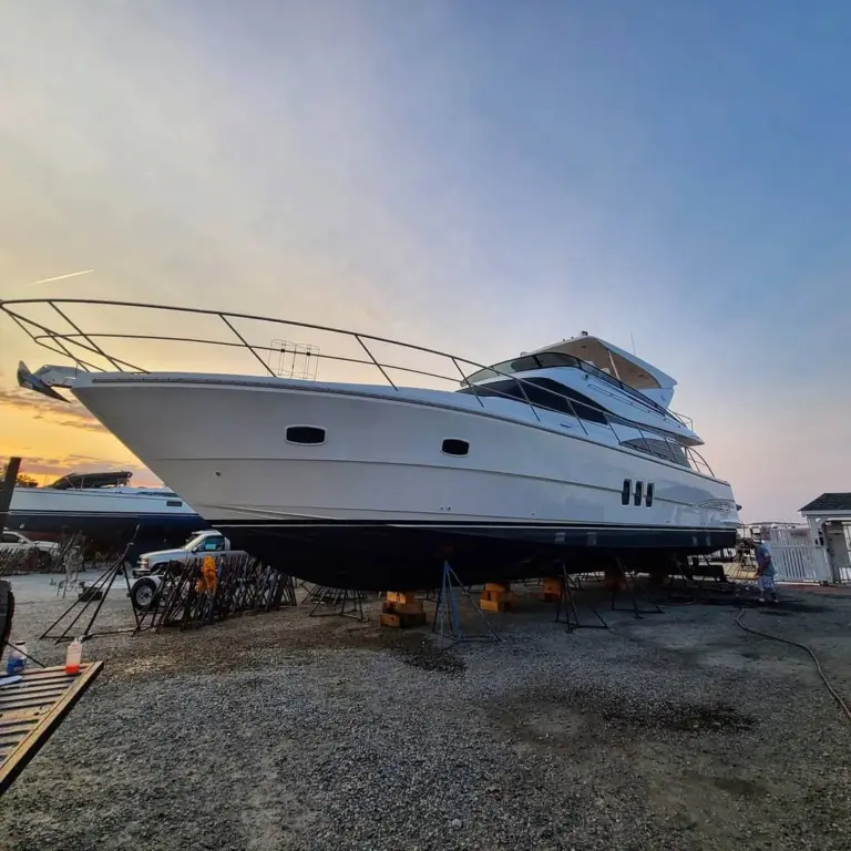White yacht elevated on supports in a dry dock facility during daytime.